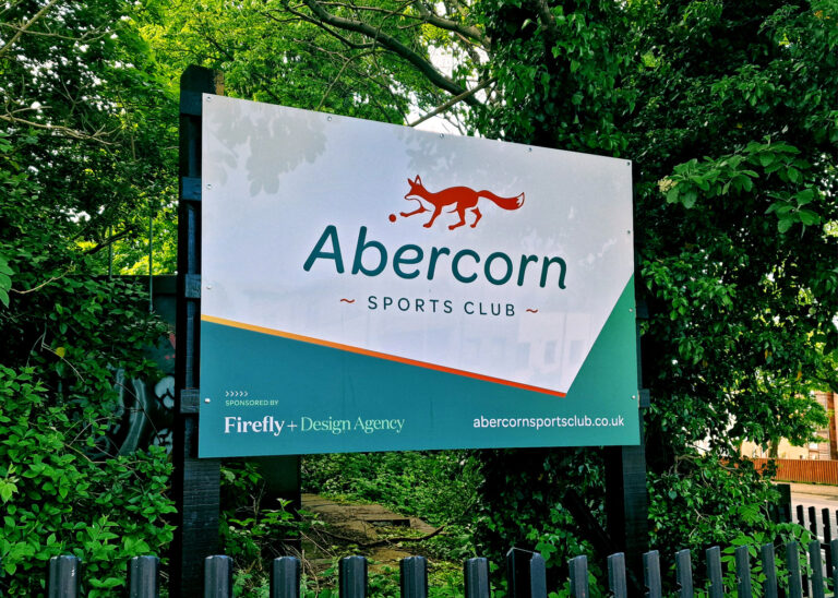 A photo of a welcome sign for the Abercorn Sports Club, featuring the fox logo and a green graphic with a "Sponsored by Firefly Design Agency" tag at the bottom.
