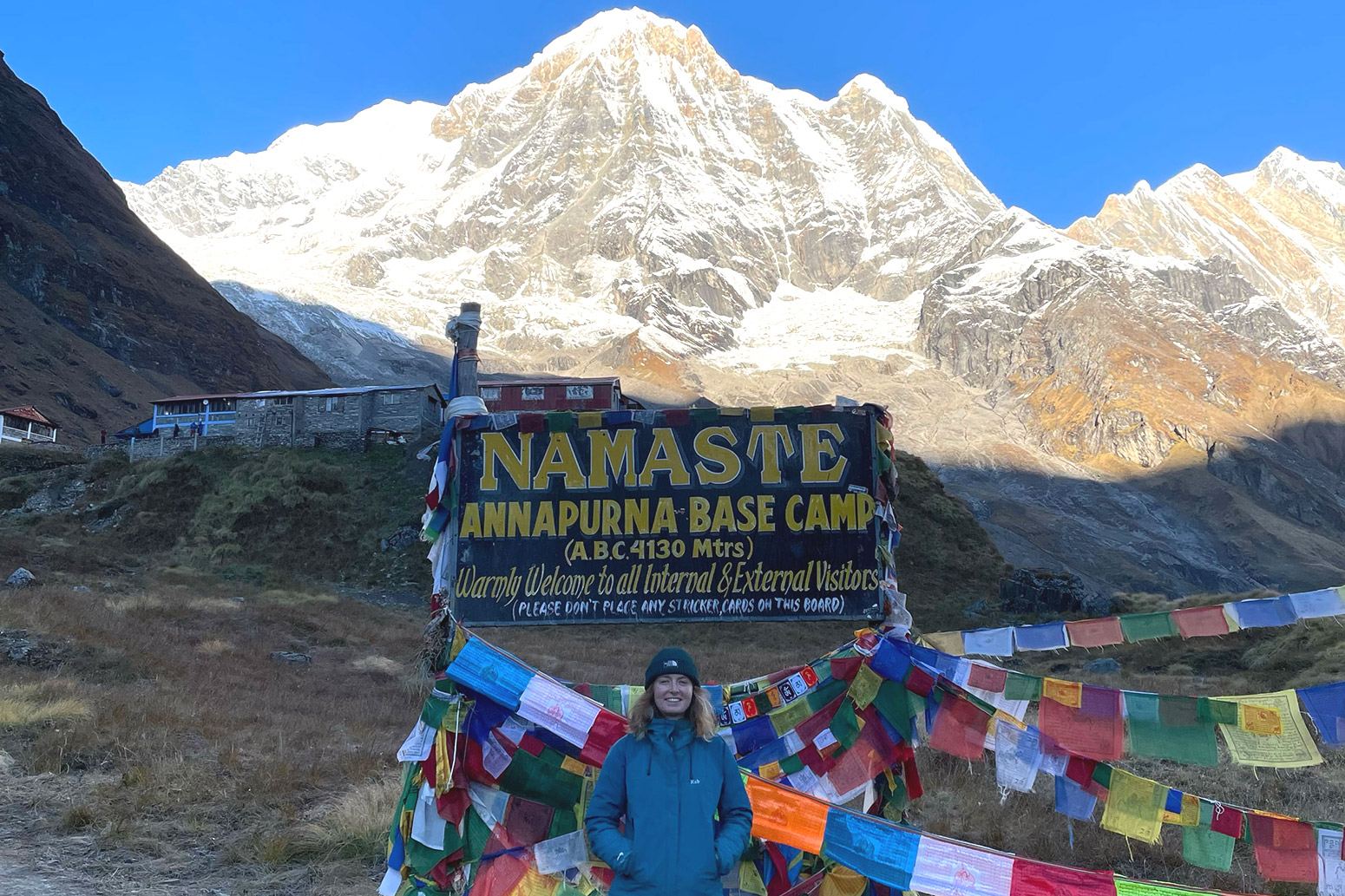 A woman standing next to the Annapurna Base Camp sign